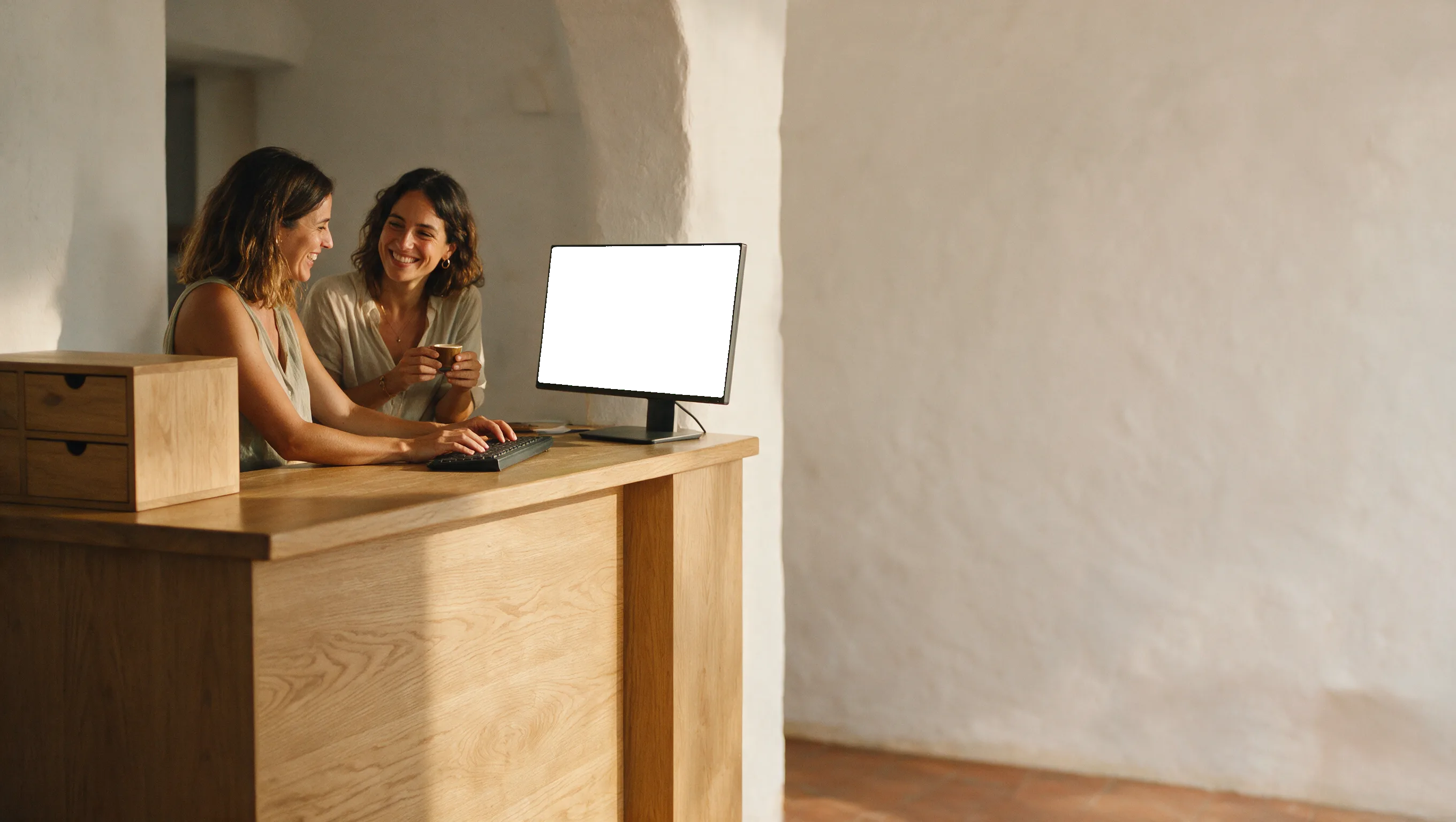 Dos recepcionistas de un hotel boutique riéndose mientras consultan el panel de Hotelgest en el mostrador